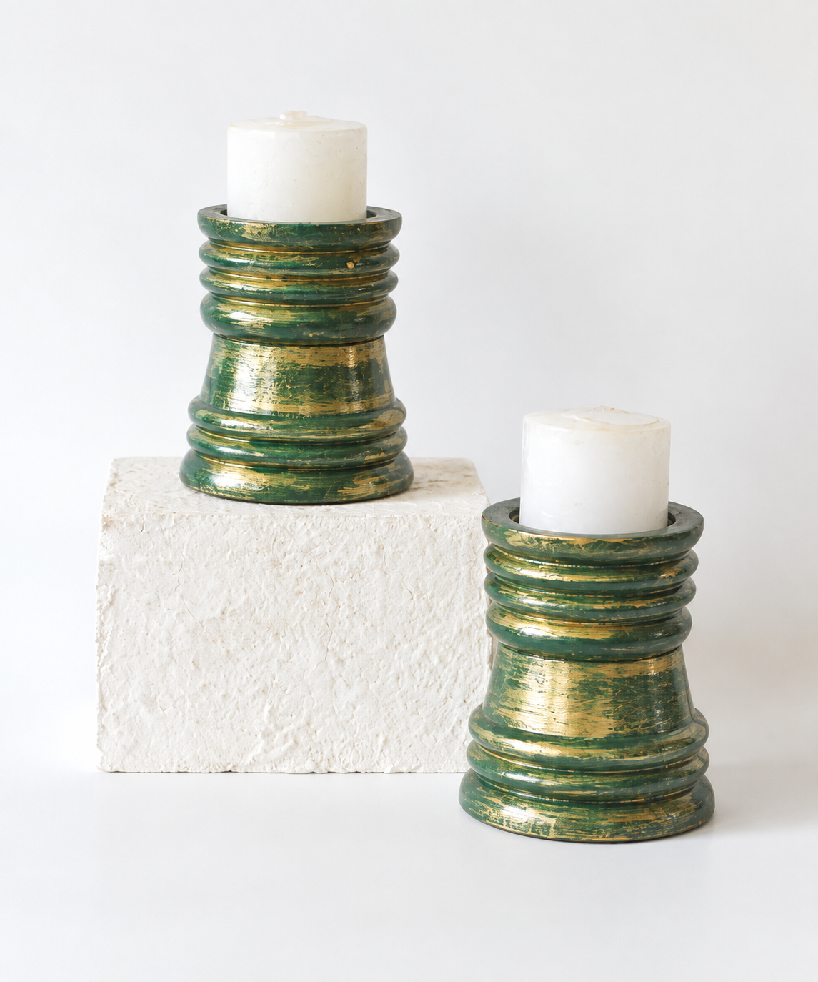 Green and gold wooden candlestands shown with white candles, hoWme.